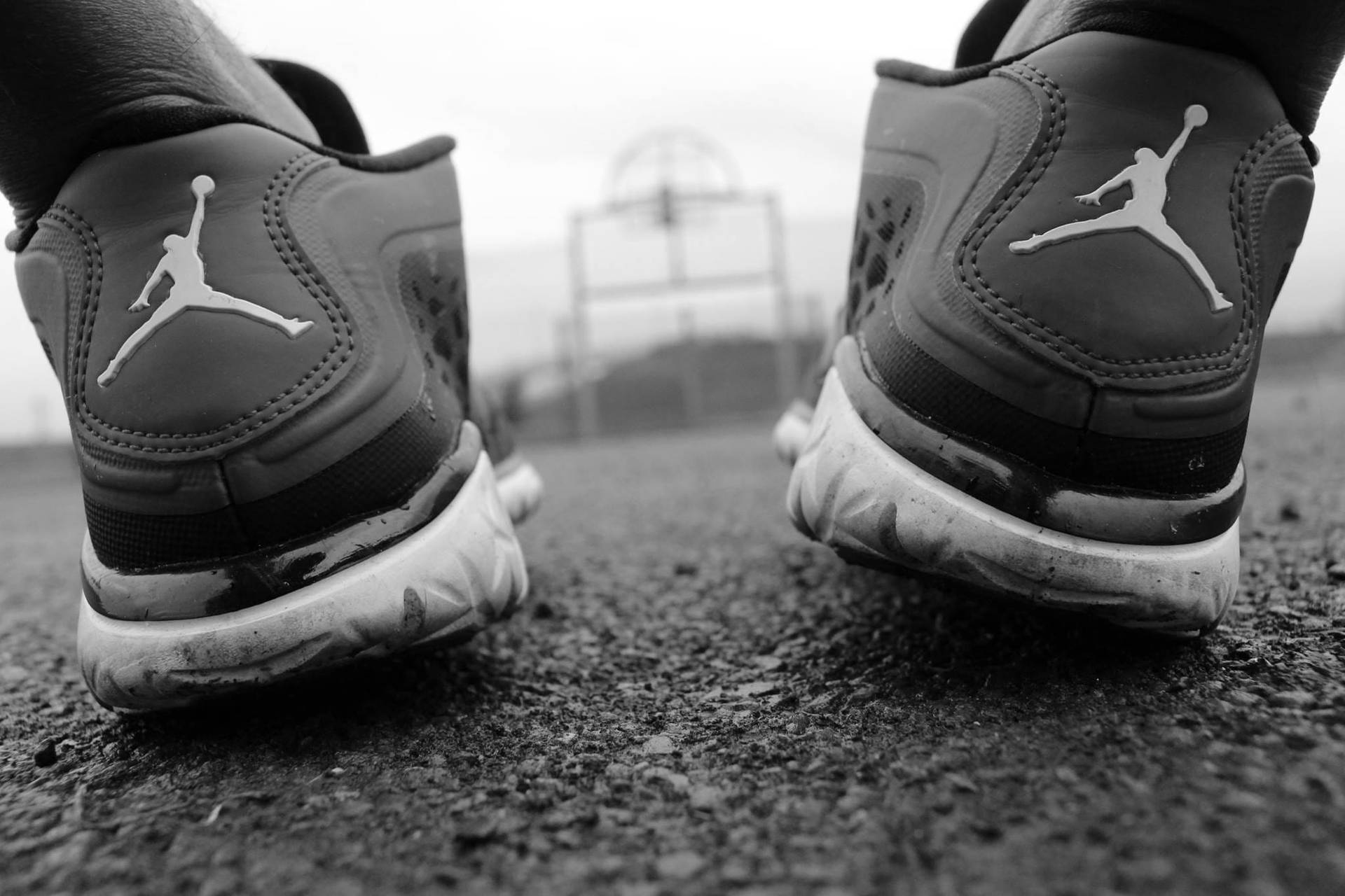 磨損的Jordan運動鞋在籃球框附近的瀝青路面上。 — Jordan Logo 壁紙