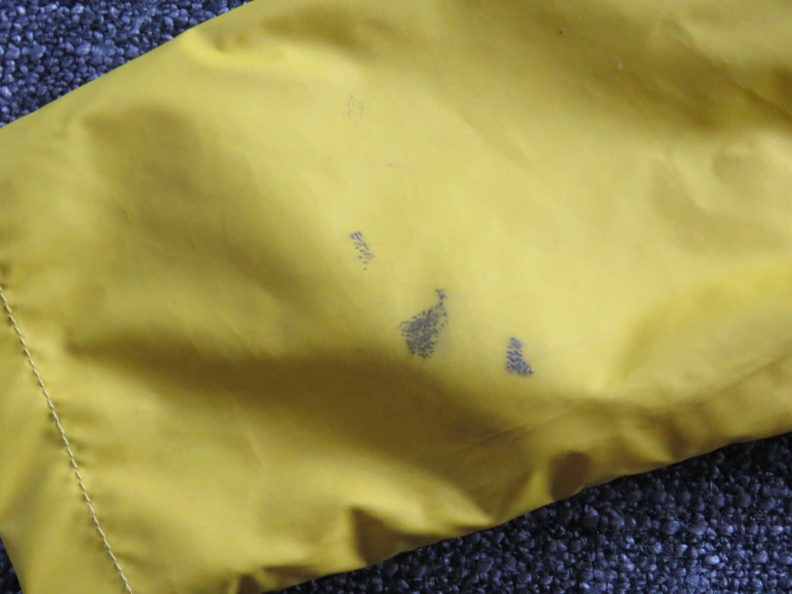 Yellow Raincoat 桌布 壁紙 — 一塊帶有深色污漬的黃色布料，放在有紋理的藍色地毯上的特寫。