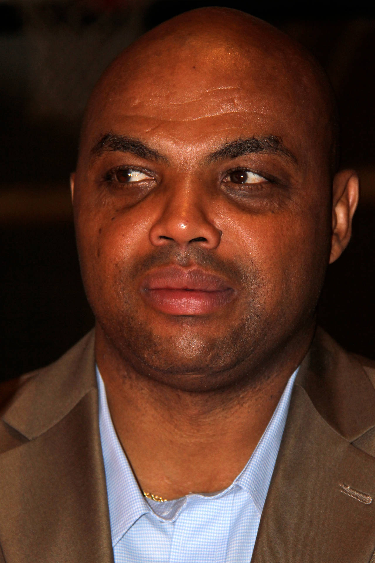 一位光頭男士身穿棕色西裝和藍色襯衫，若有所思地望向一邊。 — NBA 壁紙