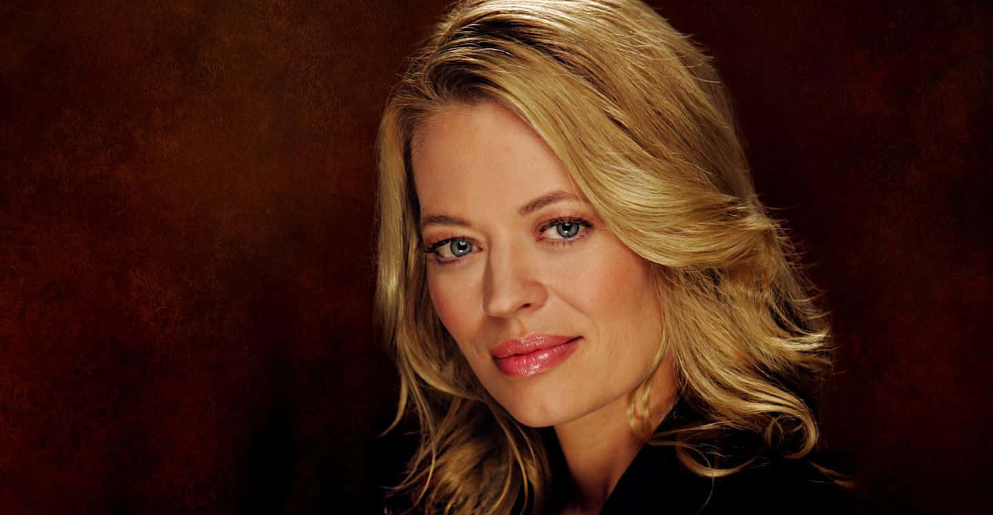 Jeri Ryan 桌布 壁紙 — 一位金髮碧眼的女人在豐富的棕色紋理背景前微笑的特寫肖像。