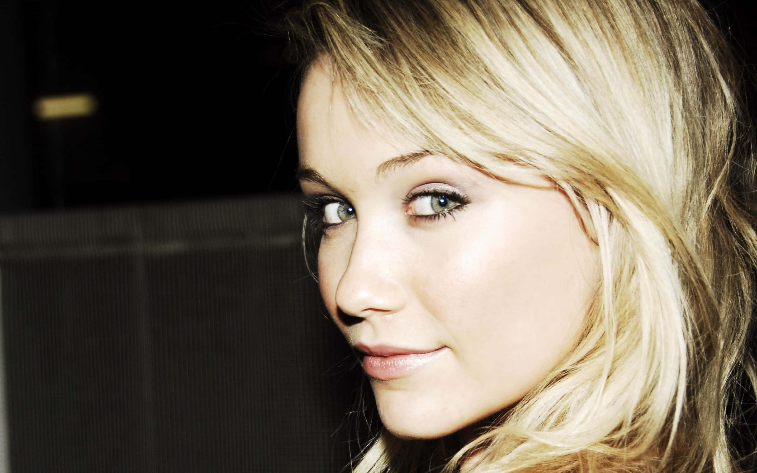 Katrina Bowden 桌布 壁紙 — 一個金髮藍眼女子的特寫肖像，她以柔和的目光凝視鏡頭，背景為深色。