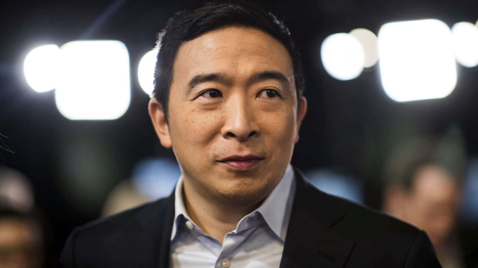 政治 桌布 壁紙 — 一個穿著西裝的男人向上看的特寫肖像，背後有明亮的燈光模糊。