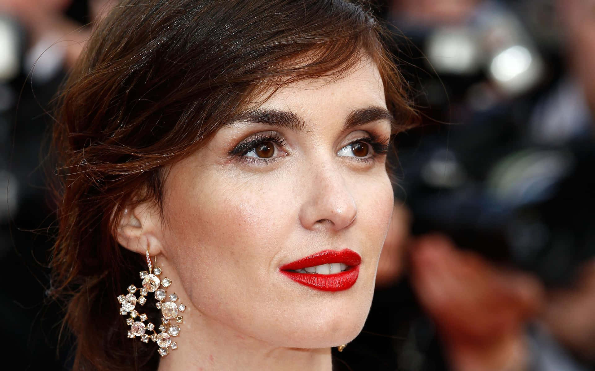 Paz Vega 桌布 壁紙 — 一位女士在華麗活動中的特寫肖像，擁有鮮豔的紅唇和閃爍的耳環。