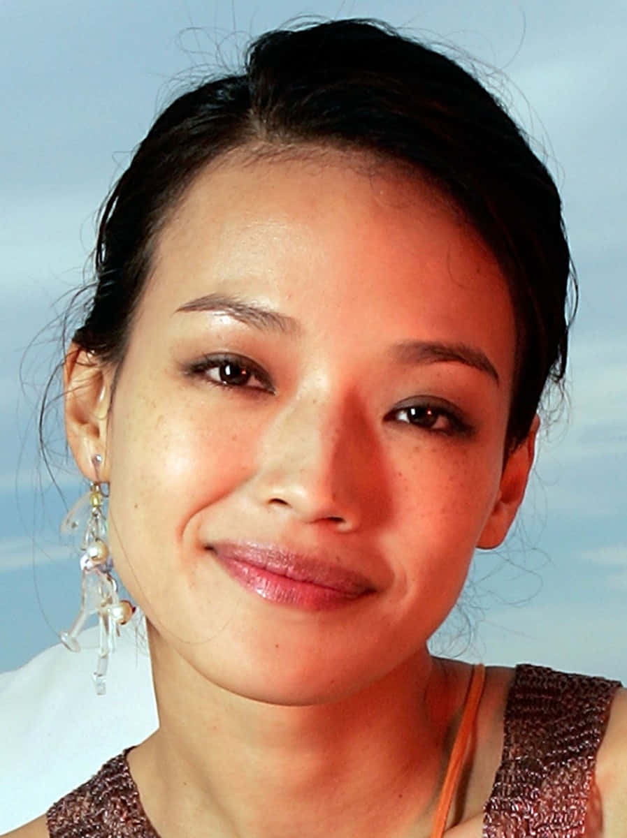 Shu Qi 桌布 壁紙 — 一位深色頭髮、戴著珍珠耳環的女性，在柔和的藍天背景下微笑的特寫肖像。