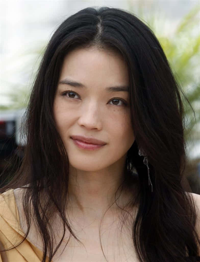 Shu Qi 桌布 壁紙 — 一位長黑髮、溫柔微笑的女性身穿黃色上衣的特寫肖像。