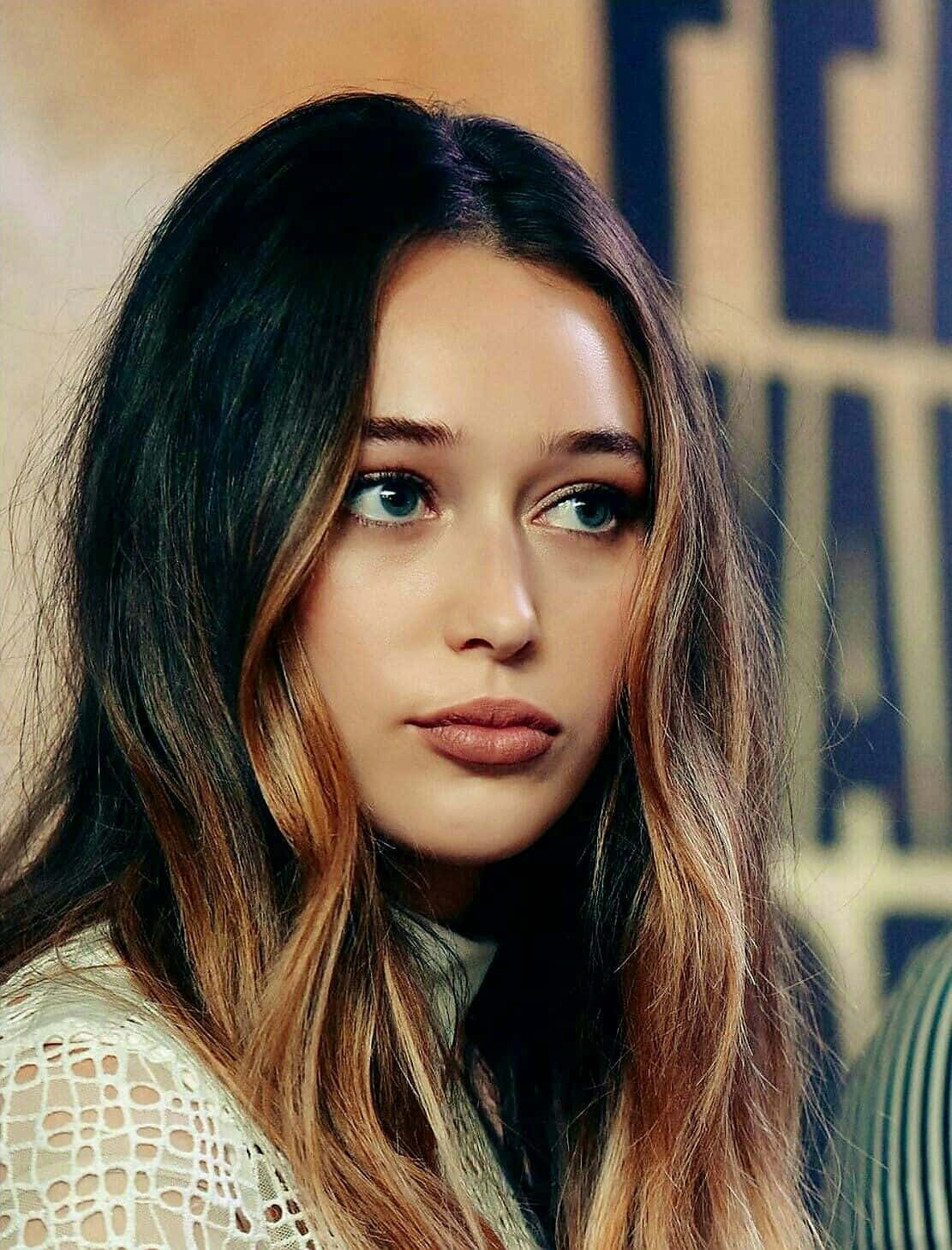 alycia debnam carey 桌布 壁紙 — 一位擁有引人注目的藍色眼睛和長長深色頭髮帶有金色挑染的女性，身穿白色蕾絲上衣的特寫肖像。