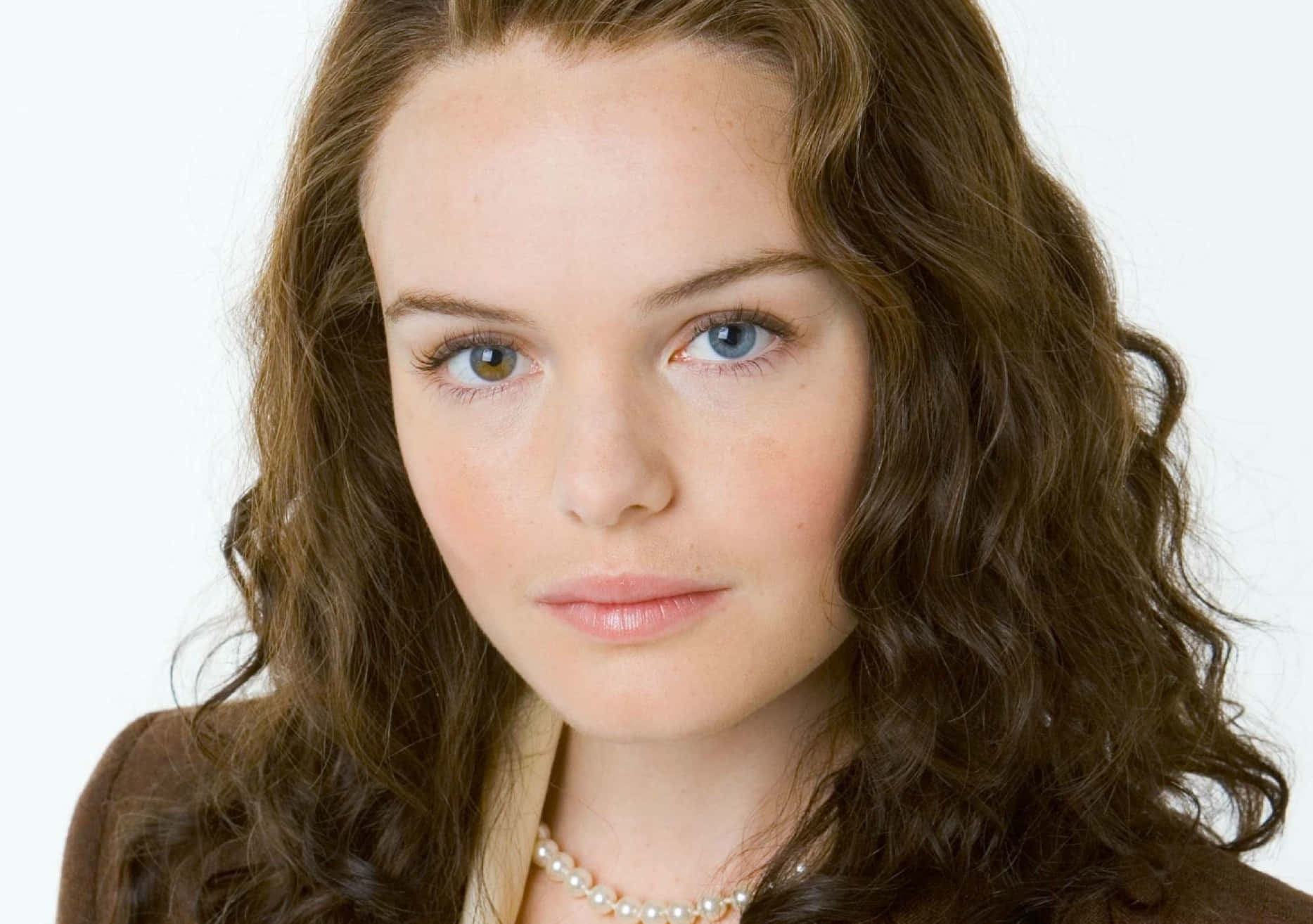 Kate Bosworth 桌布 壁紙 — 一位年輕女性的特寫肖像，擁有引人注目的虹膜異色症和波浪形棕色頭髮，背景為純白色。