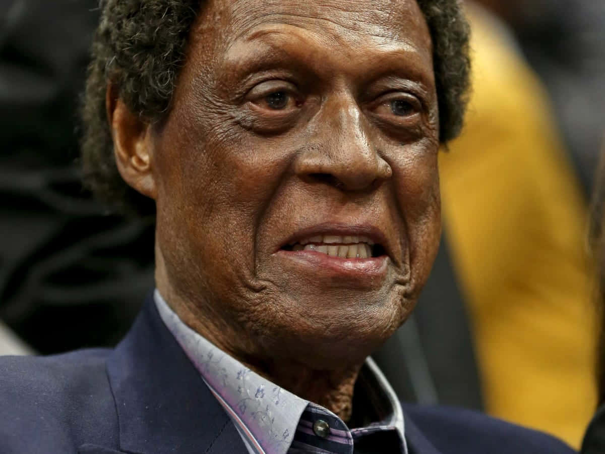 年長黑人男性穿著西裝和圖案襯衫微笑。 — NBA 壁紙