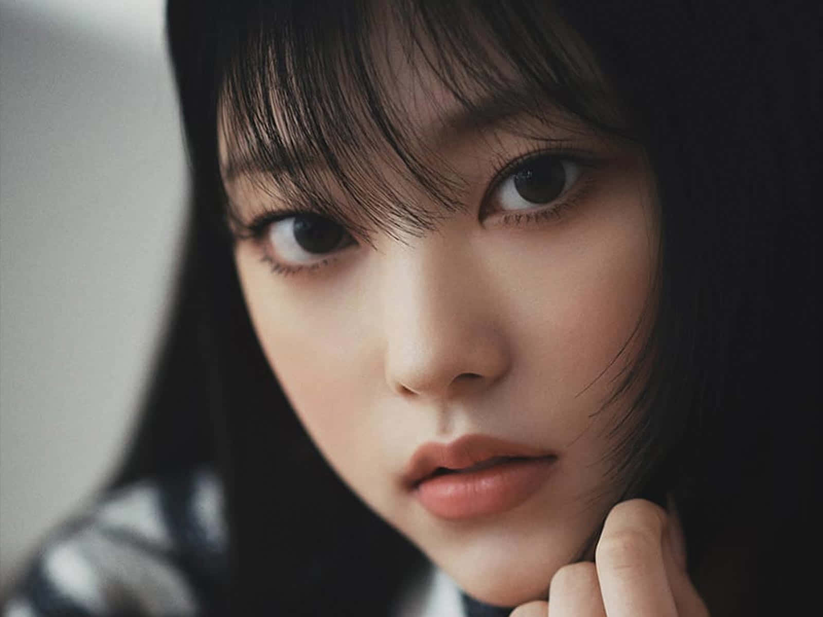  壁紙 — 一位年輕黑髮女子的特寫肖像，她眼神專注，直視鏡頭，一隻手輕柔地靠近下巴。