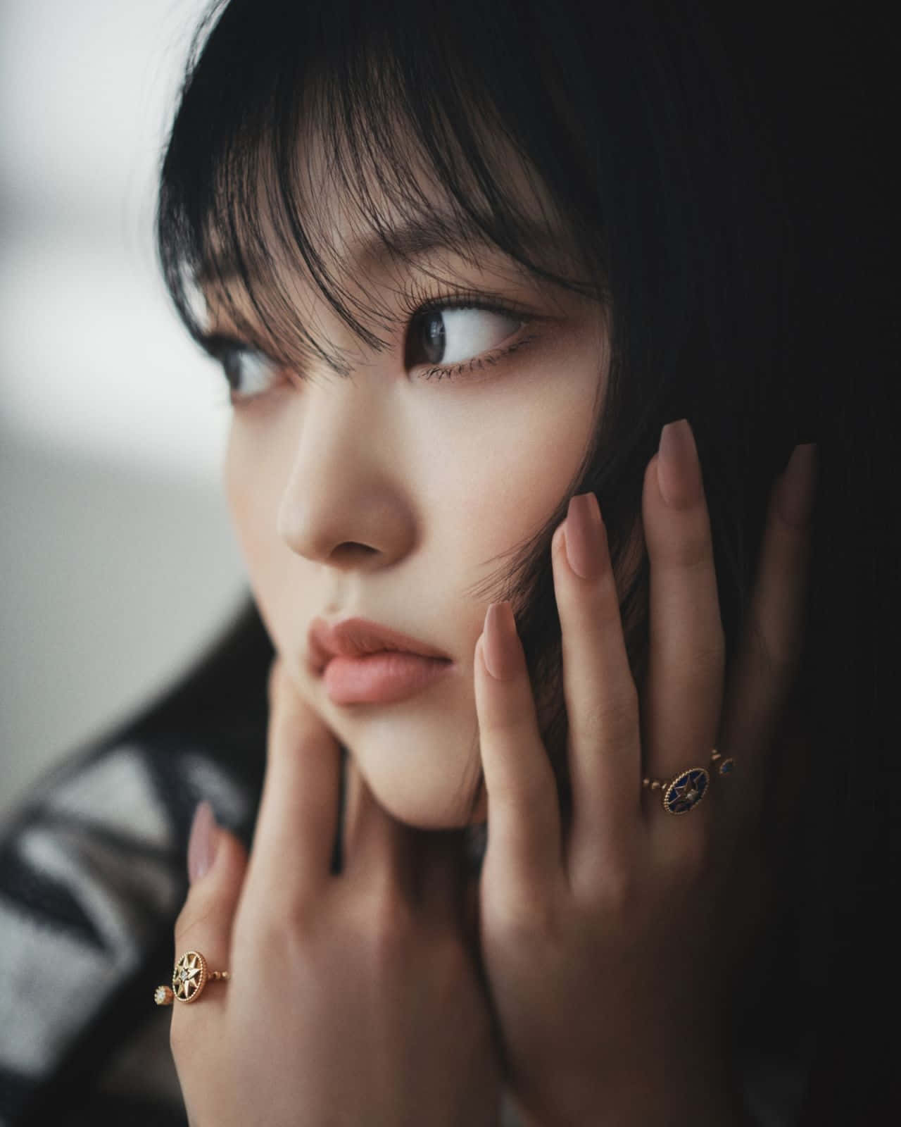  壁紙 — 一位深色頭髮、化著淡妝的年輕女性，戴著珠寶戒指輕輕觸碰臉龐，若有所思地凝視著的近距離肖像。