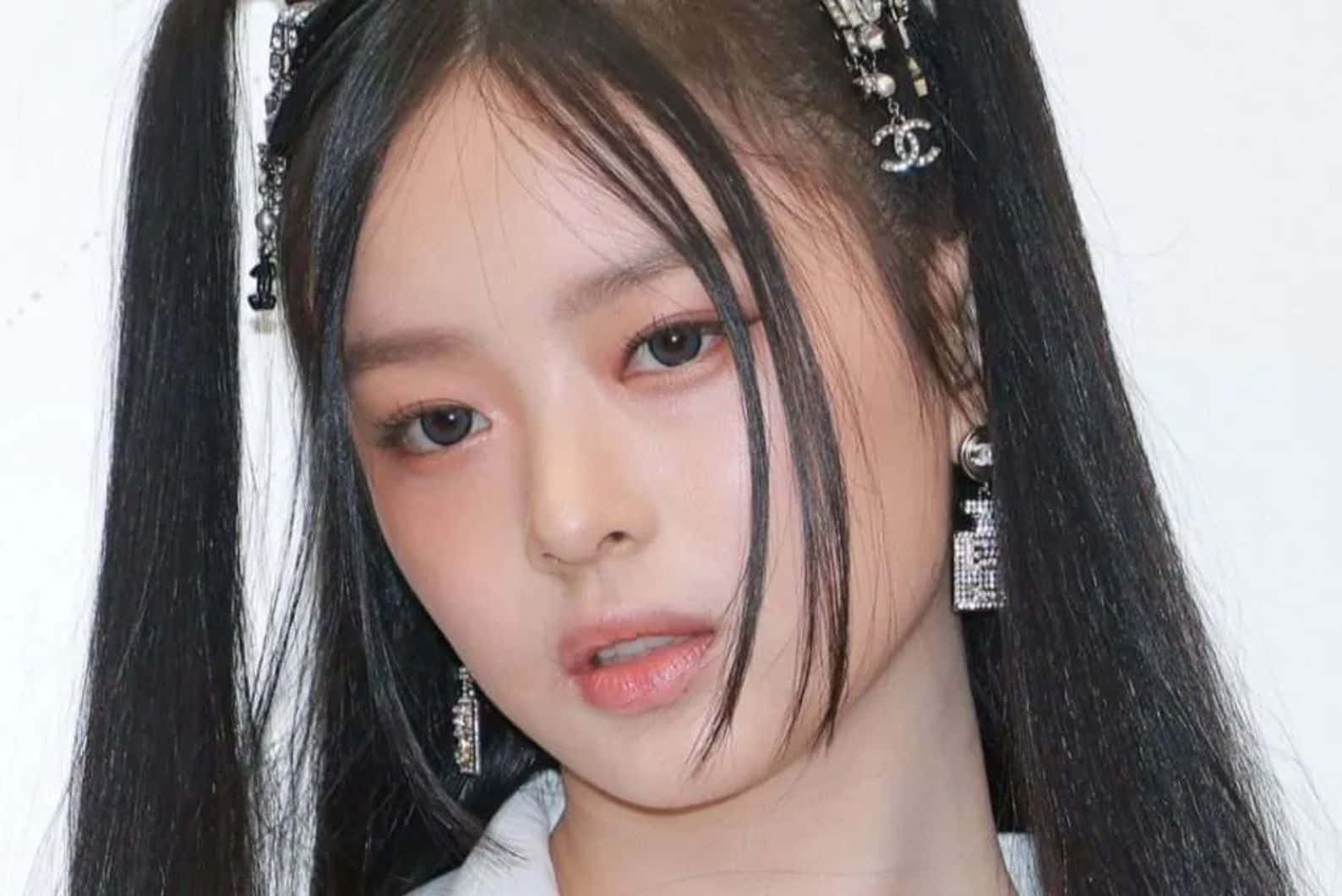  壁紙 — 一位年輕女性的特寫肖像，長長的黑髮上點綴著 Chanel 髮夾和閃閃發光的香水瓶耳環。