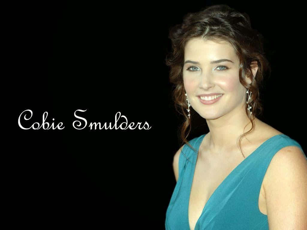Cobie Smulders 桌布 壁紙 — Cobie Smulders 在黑色背景前，身穿藍綠色連衣裙，溫暖微笑，她的名字用白色字體寫出。