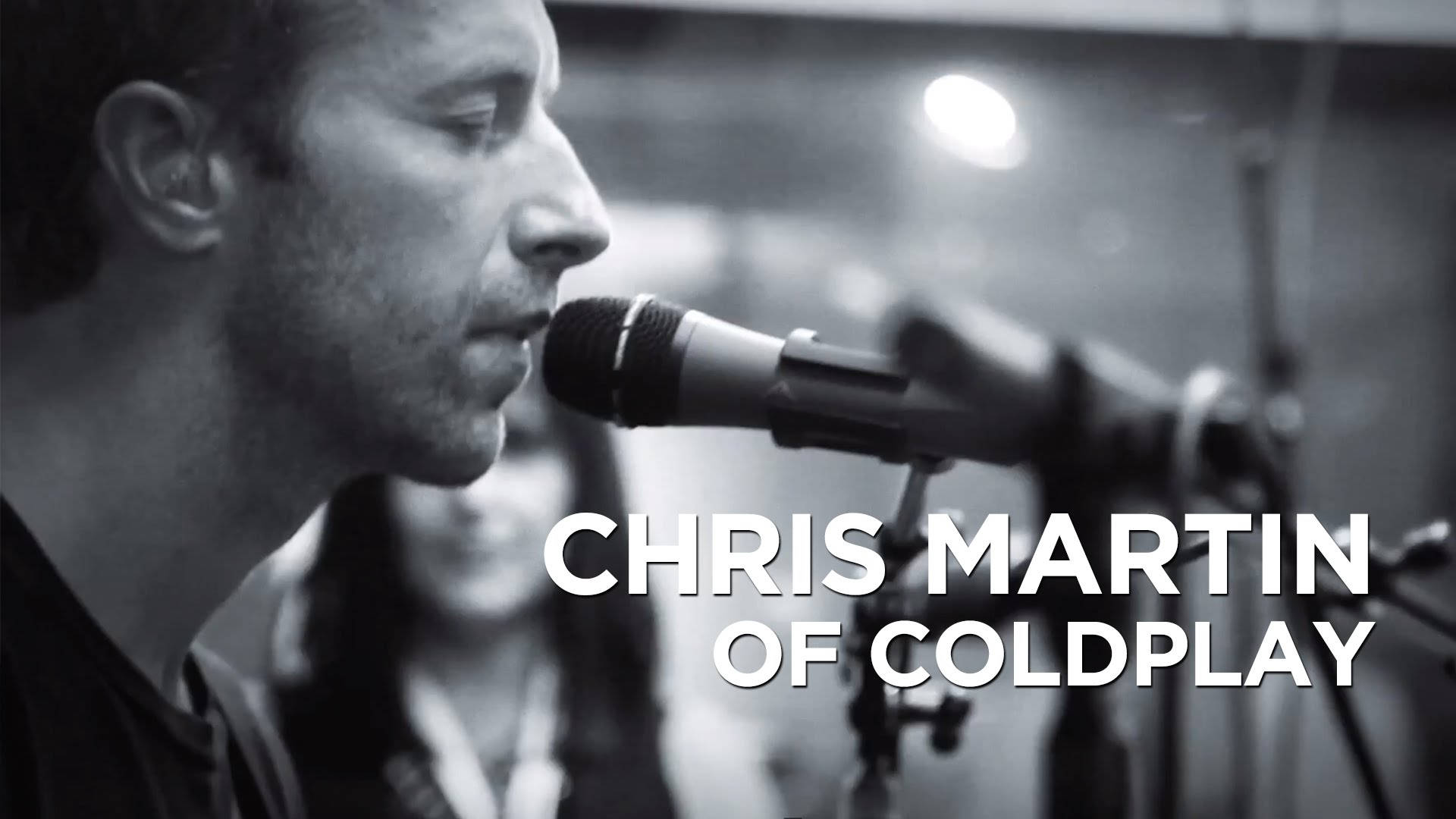 Chris Martin 桌布 壁紙 — Coldplay 的 Chris Martin 在光線昏暗、柔和燈光及模糊背景的錄音室中對著麥克風唱歌。