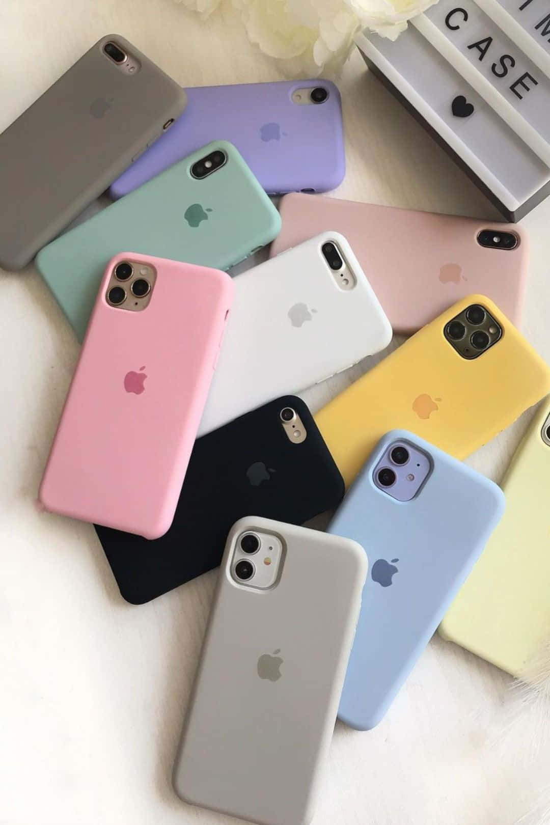 在白色表面上，一系列色彩繽紛的iPhone保護殼，包括粉彩和純色調。 — iPhone 13 Pro Max 壁紙