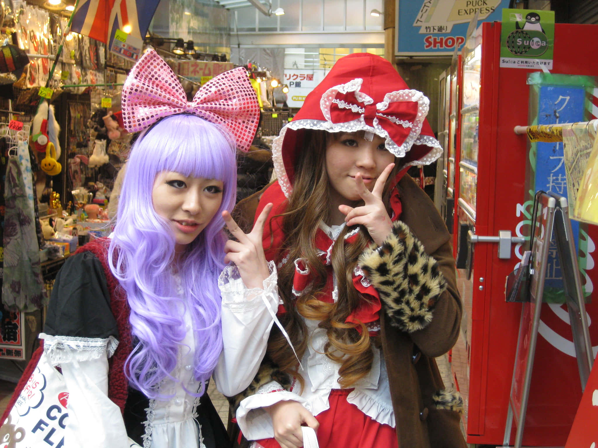 Harajuku Fashion 桌布 壁紙 — 兩位年輕女性穿著色彩繽紛的cosplay服裝，在熱鬧的日本購物拱廊中愉快地擺姿勢。