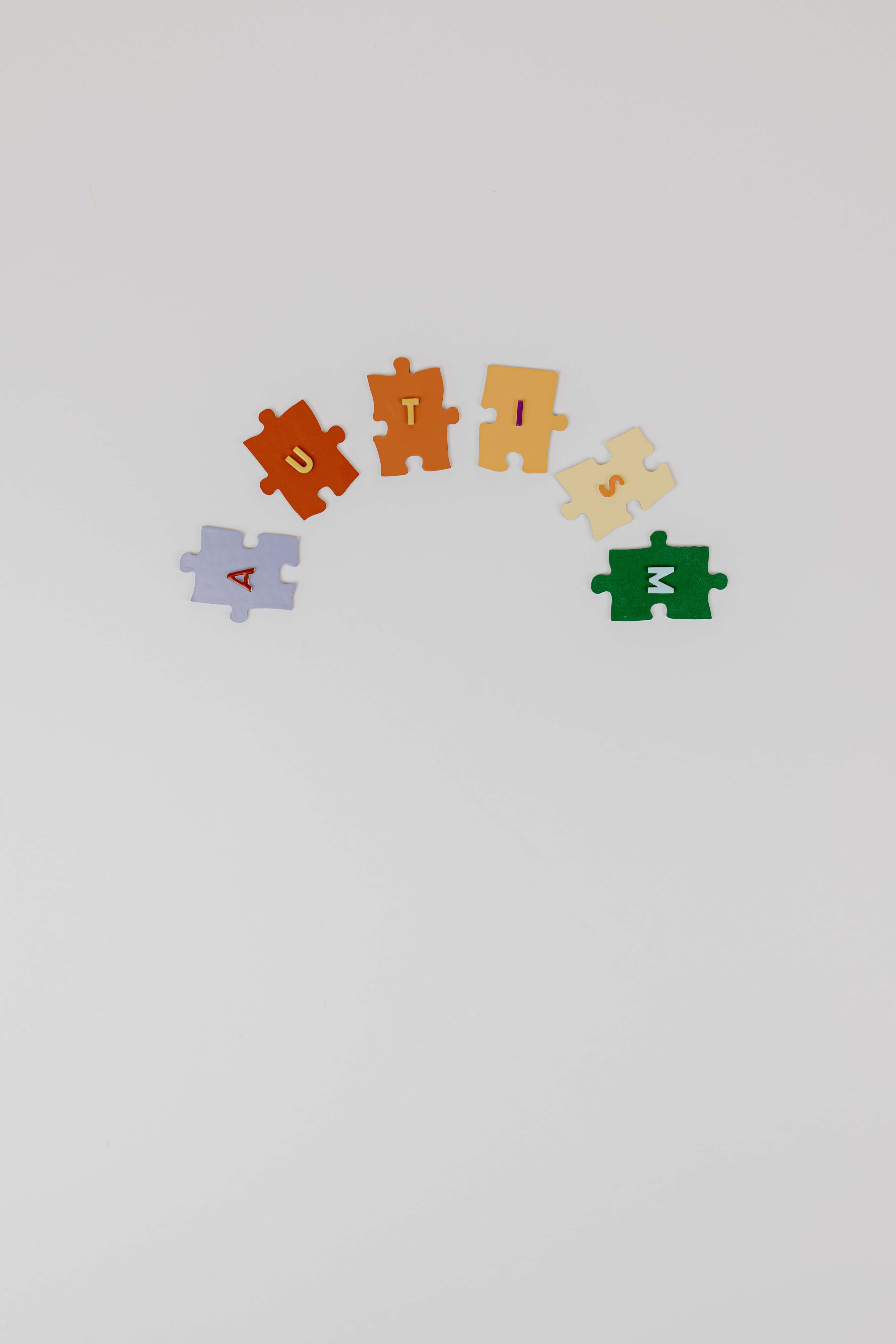 Autism 桌布 壁紙 — 色彩繽紛的拼圖塊拼出自閉症一詞，以柔和弧線排列在純白表面上。