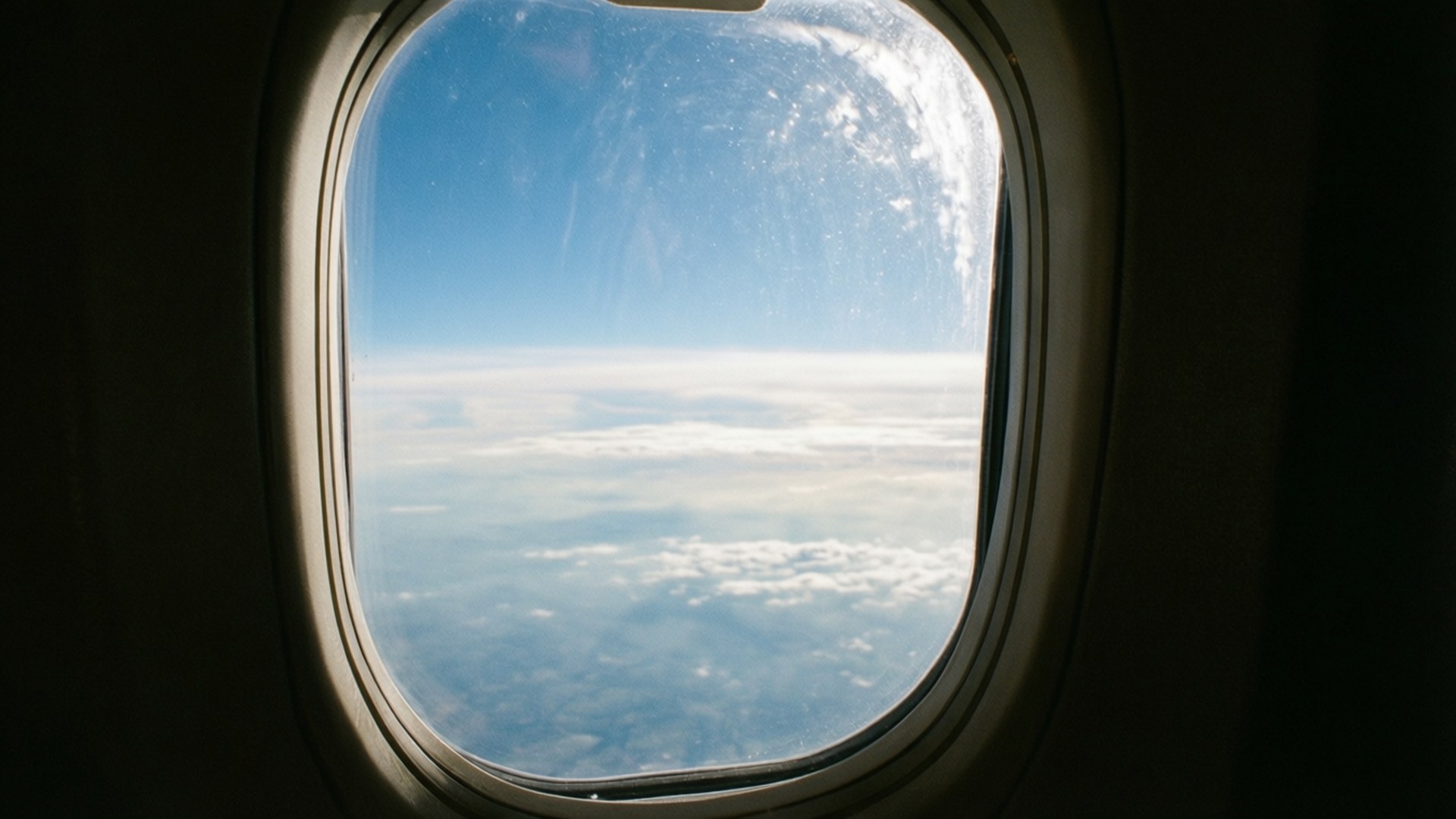 Airplane Window Sky View 壁紙 — 從飛機窗戶看到的景色顯示出廣闊的藍天，下方是一片蓬鬆的白雲海。