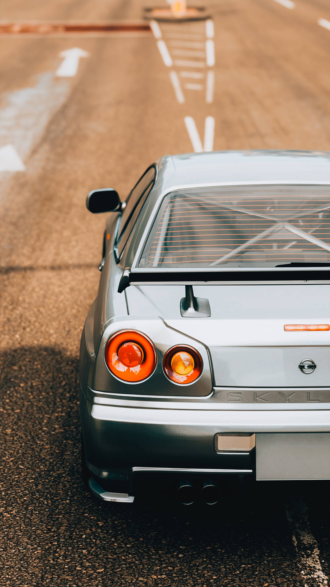銀色日產Skyline R32跑車在鋪砌道路上，帶有白色車道標線。 — 日產Skyline GTR R33壁紙 壁紙