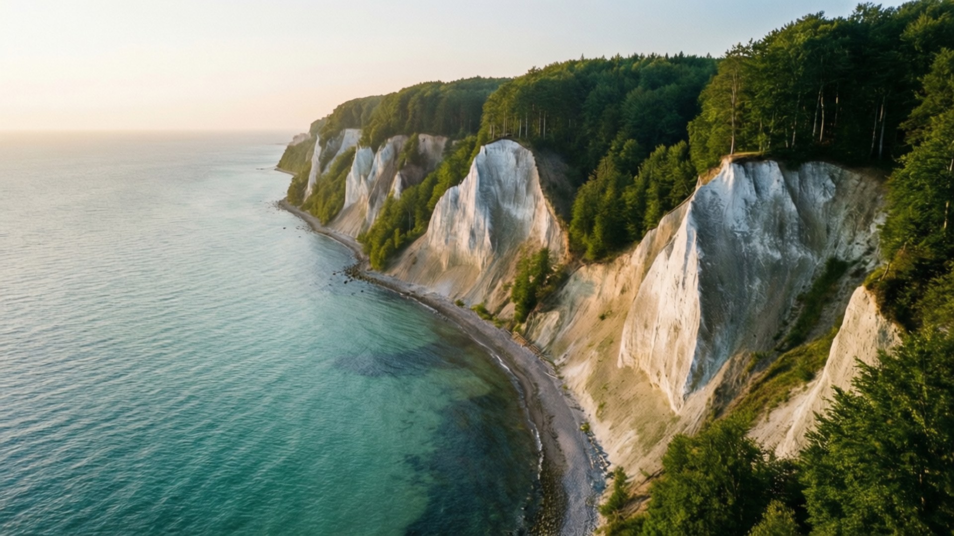 Møns Klint Sunrise 壁紙 — 從空中俯瞰戲劇性的白色白堊懸崖，覆蓋著綠色森林，俯瞰金色時刻的碧綠海洋。