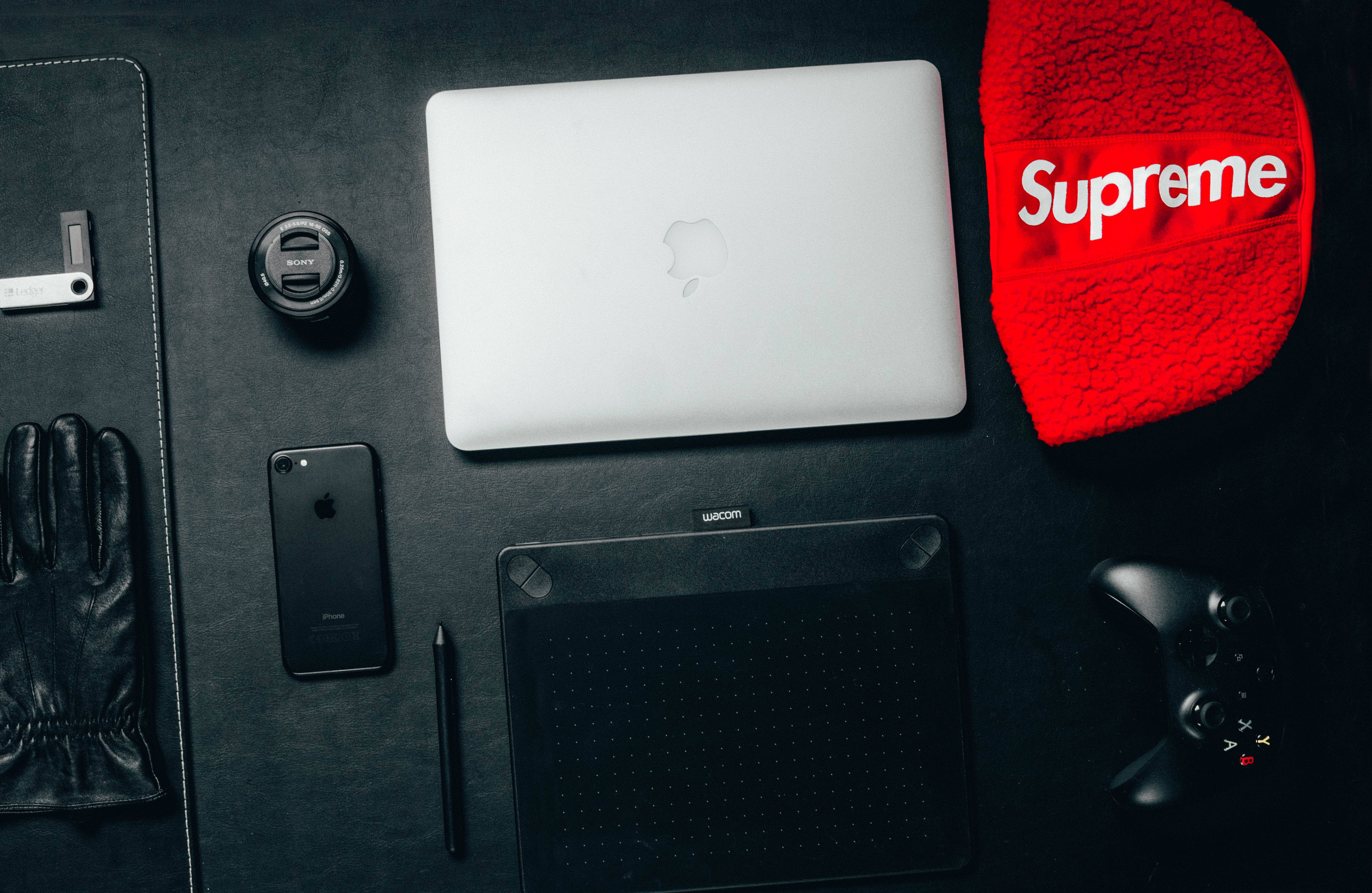 科技設備和遊戲配件排列在深色桌子上，配有一頂紅色毛帽。 — Macbook Pro 壁紙