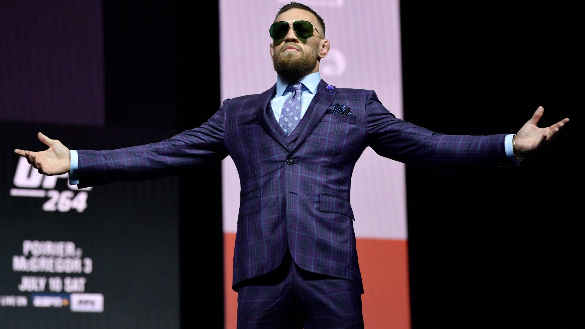 Mcgregor 桌布 壁紙 — Conor McGregor 在UFC活動中自信地站在舞台上，身穿紫色格紋西裝和太陽眼鏡，雙臂張開。