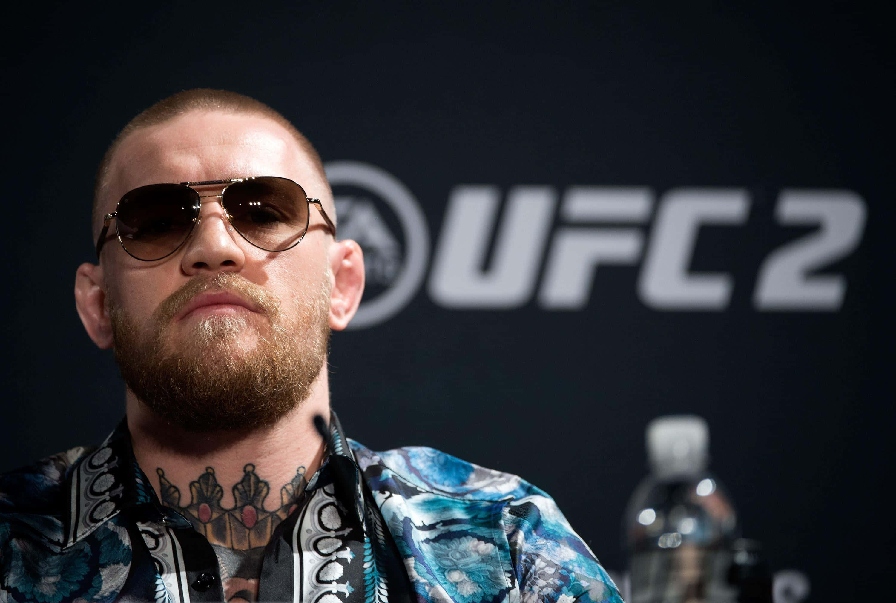 康納·麥葛雷格 桌布 壁紙 — Conor McGregor 在 UFC 2 記者會上戴著飛行員太陽眼鏡和圖案襯衫，背景為黑色。