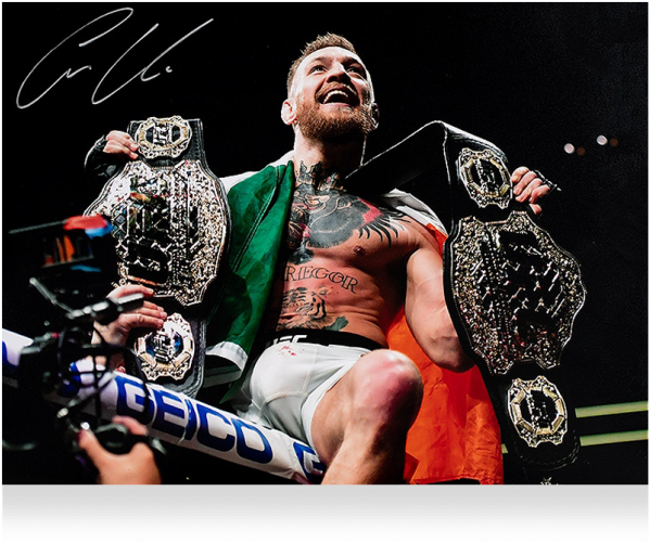 康納·麥葛雷格 桌布 壁紙 — Conor McGregor 在八角籠中勝利慶祝，手持兩條冠軍腰帶，肩上披著綠色和橙色的布。