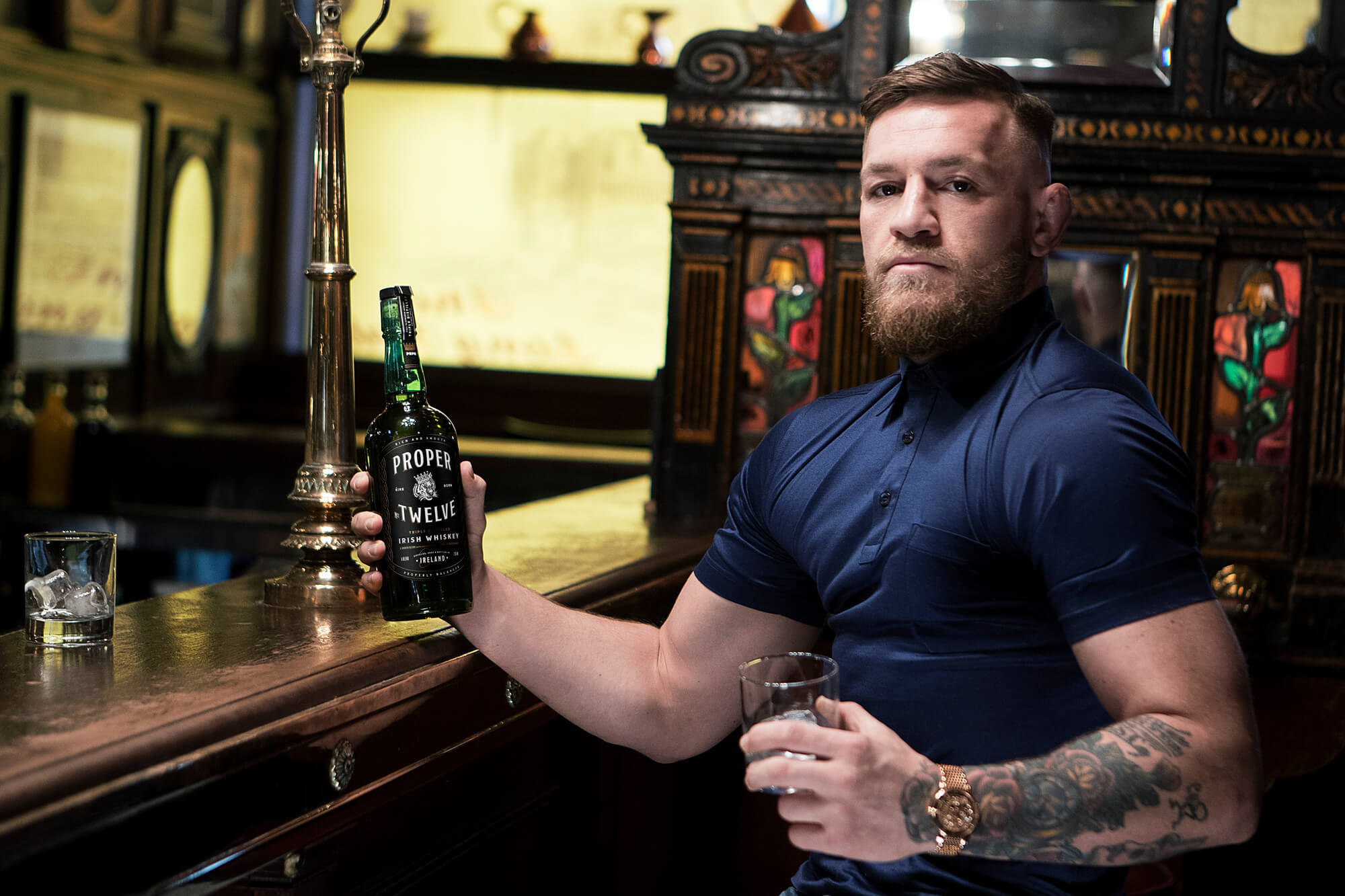 Mcgregor 桌布 壁紙 — Conor McGregor 坐在復古酒吧，手持一瓶Proper Twelve愛爾蘭威士忌和一杯加冰的威士忌。