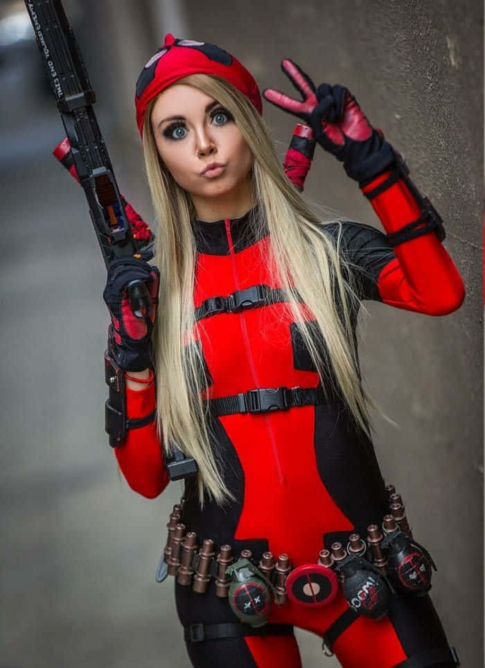 Lady Deadpool 桌布 壁紙 — 一位Cosplayer穿著紅黑色死侍服裝，拿著道具槍並比出和平手勢，以混凝土牆為背景擺姿勢。