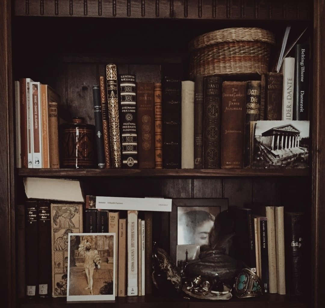 Dark Book Aesthetic 桌布 壁紙 — 一個舒適的復古書架，放滿了皮革裝訂的經典書籍、編織籃子和在溫暖琥珀色燈光下的棕褐色照片。
