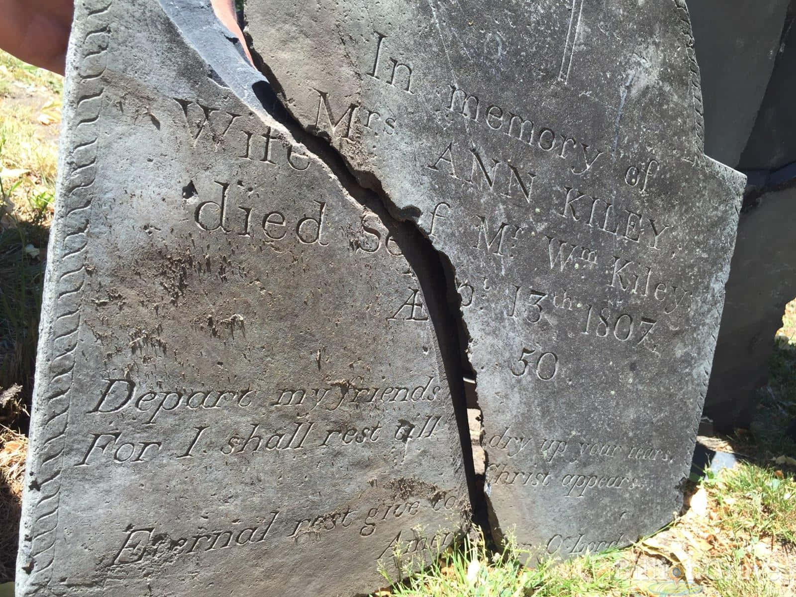 Gravestone 桌布 壁紙 — 一塊裂開且風化的墓碑，刻有女性名字和墓誌銘，矗立在陽光明媚的草地上。