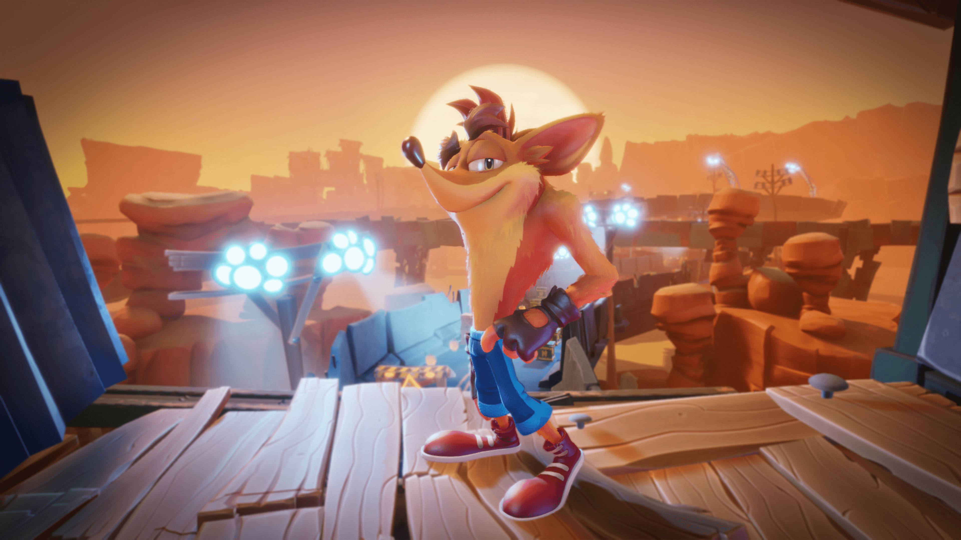 Bandicoot 桌布 壁紙 — Crash Bandicoot 自信地站在沙漠峽谷中的木製平台上，夕陽西下，身後有發光的藍色燈光。