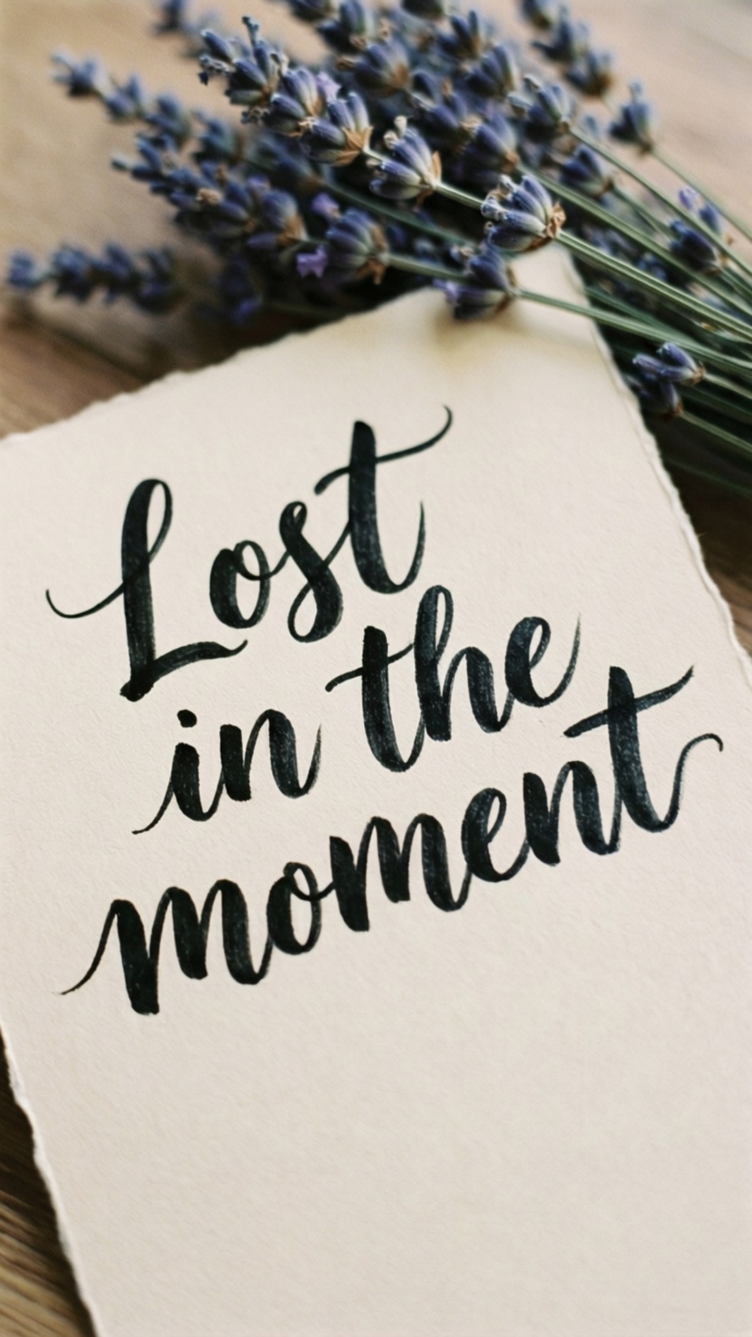 Lost in the Moment 壁紙 — 一張米色紙上以黑色書法寫著「Lost in the moment」，旁邊放著乾燥薰衣草在木質表面上。