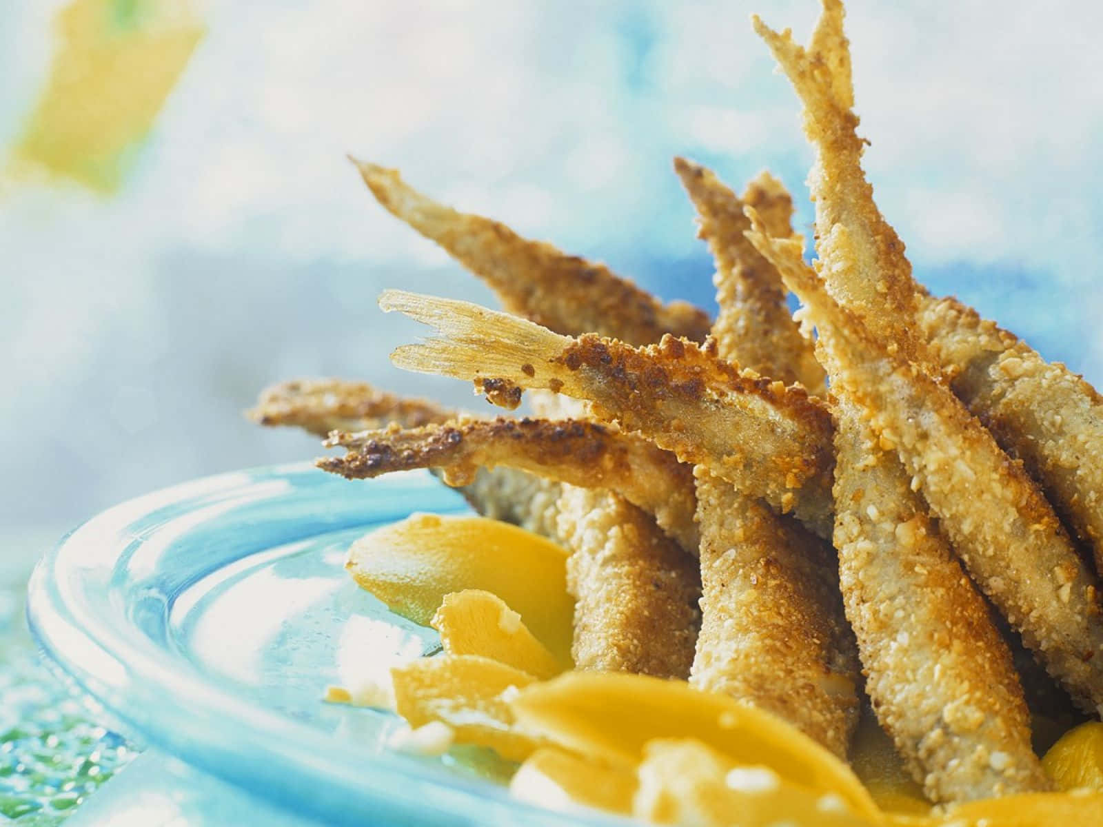  壁紙 — 脆炸鯷魚高高堆放在藍色盤子上，配上檸檬角，背景柔和模糊。