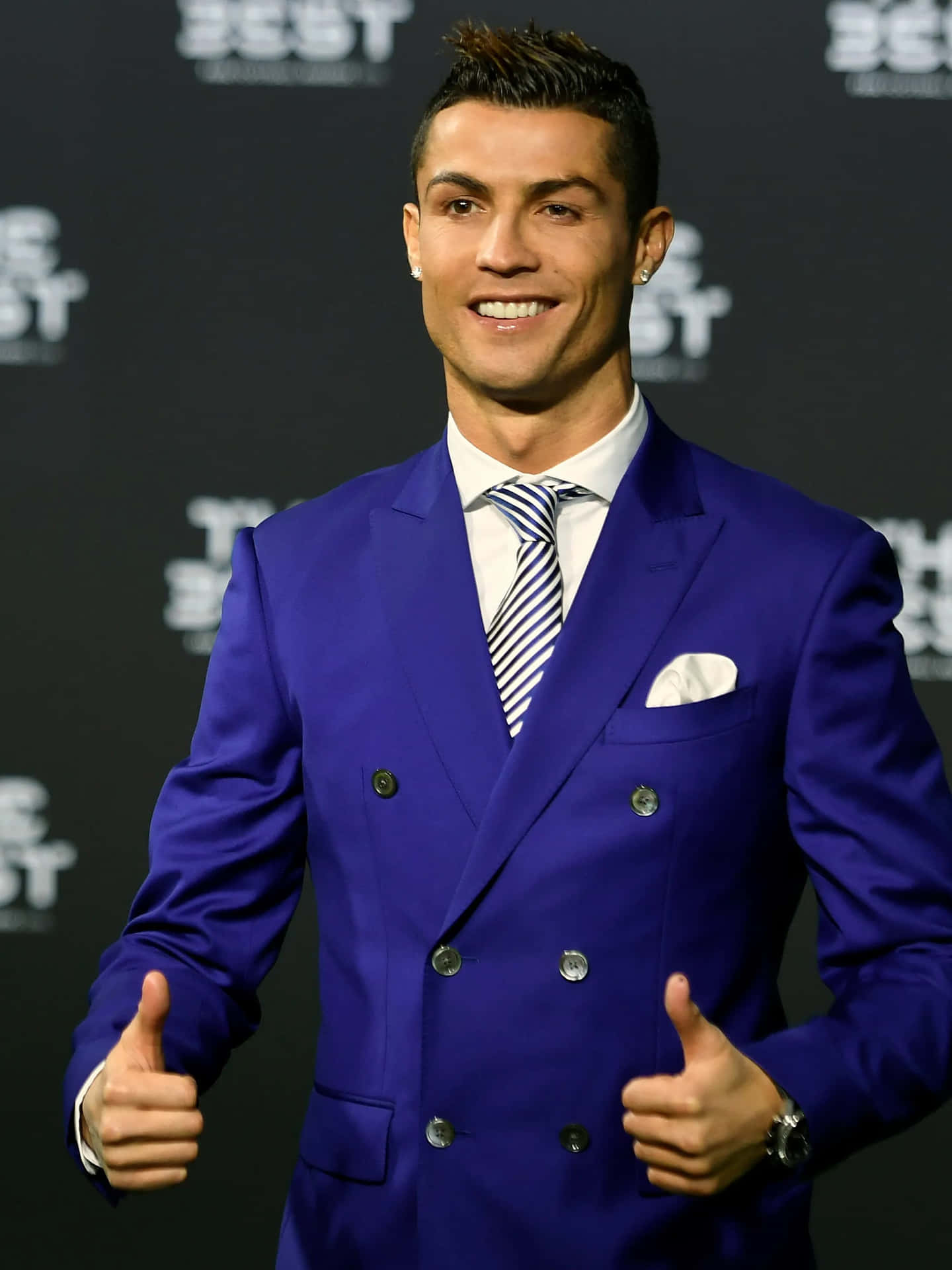 壁紙 — Cristiano Ronaldo 穿著大膽的藍色雙排扣西裝，自信微笑，在正式活動中豎起兩個大拇指。