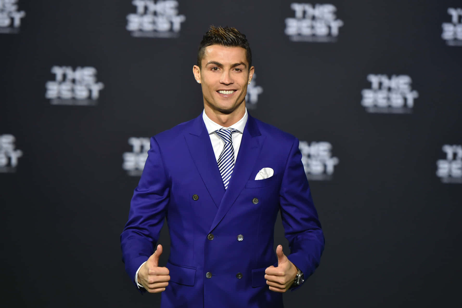  壁紙 — Cristiano Ronaldo 穿著一套剪裁俐落的皇家藍雙排扣西裝，自信微笑，在「The Best」活動中豎起兩個大拇指。