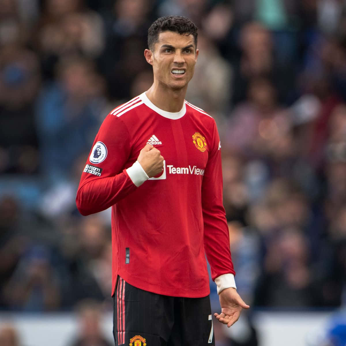 克里斯蒂亞諾·羅納度 桌布 壁紙 — Cristiano Ronaldo 身穿紅色曼聯球衣，在比賽中握緊拳頭，背景是模糊的球場人群。