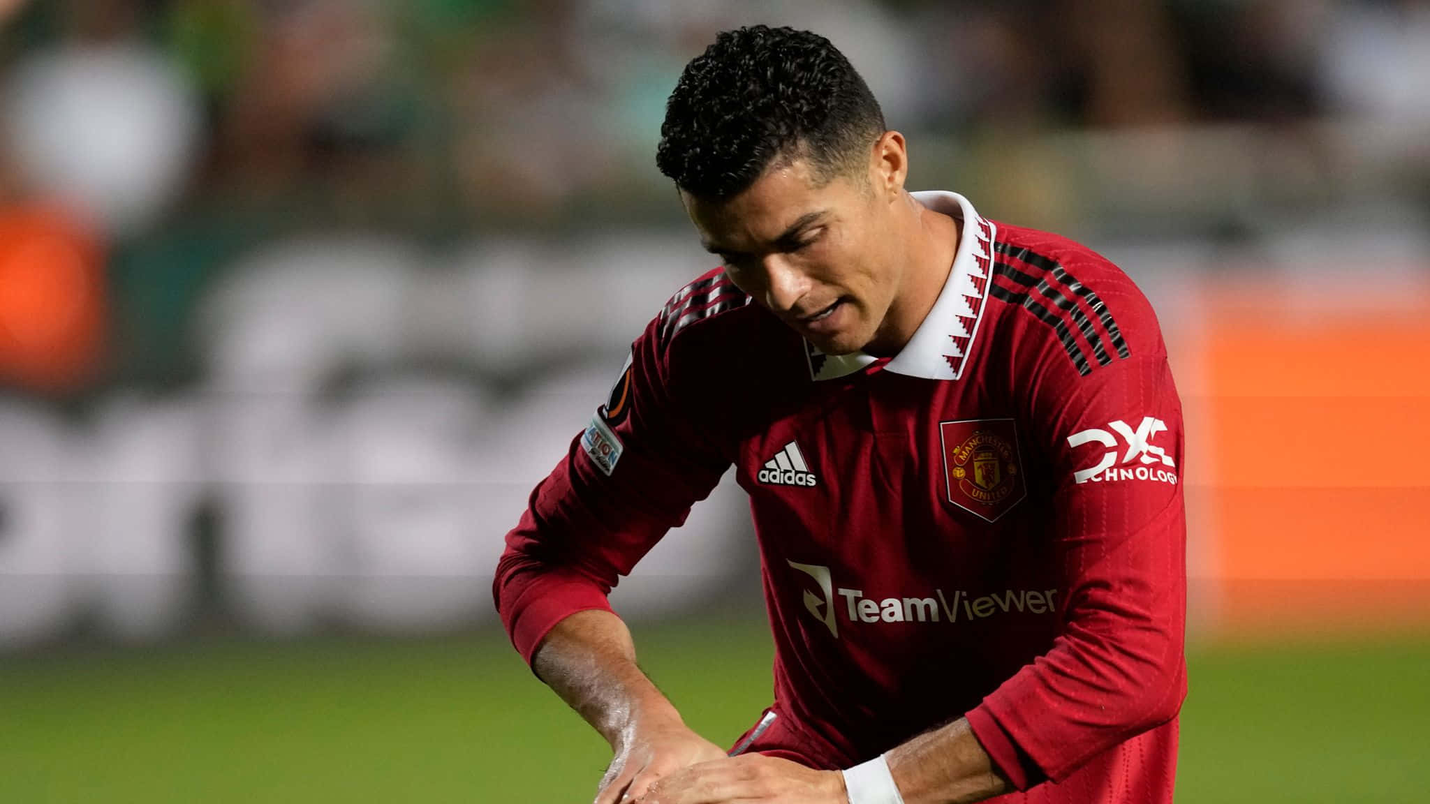 克里斯蒂亞諾·羅納度 桌布 壁紙 — Cristiano Ronaldo 身穿紅色曼聯球衣，在球場燈光下專注地低頭看著綠色足球場。