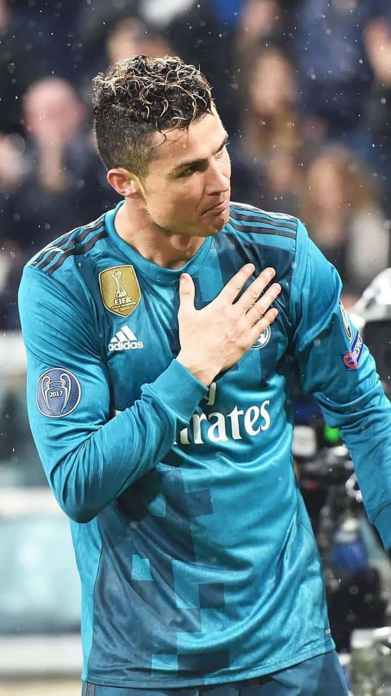  壁紙 — Cristiano Ronaldo 身穿藍色皇家馬德里球衣，在雨中的足球比賽中，在球場燈光下將手放在心口上。