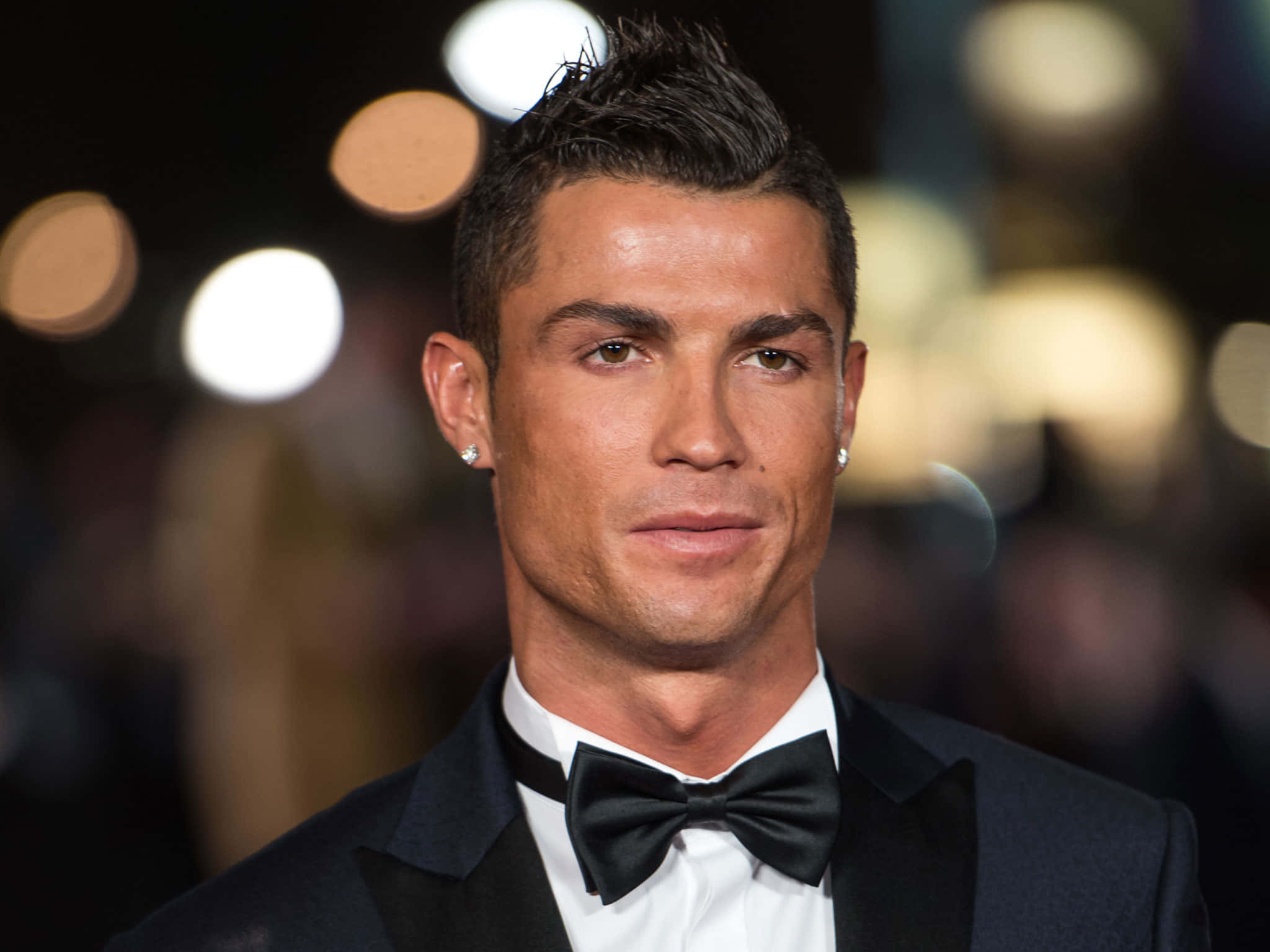 Ronaldo 桌布 壁紙 — Cristiano Ronaldo 身穿俐落黑色禮服和領結，在柔和模糊的夜間燈光背景下自信地凝視鏡頭。