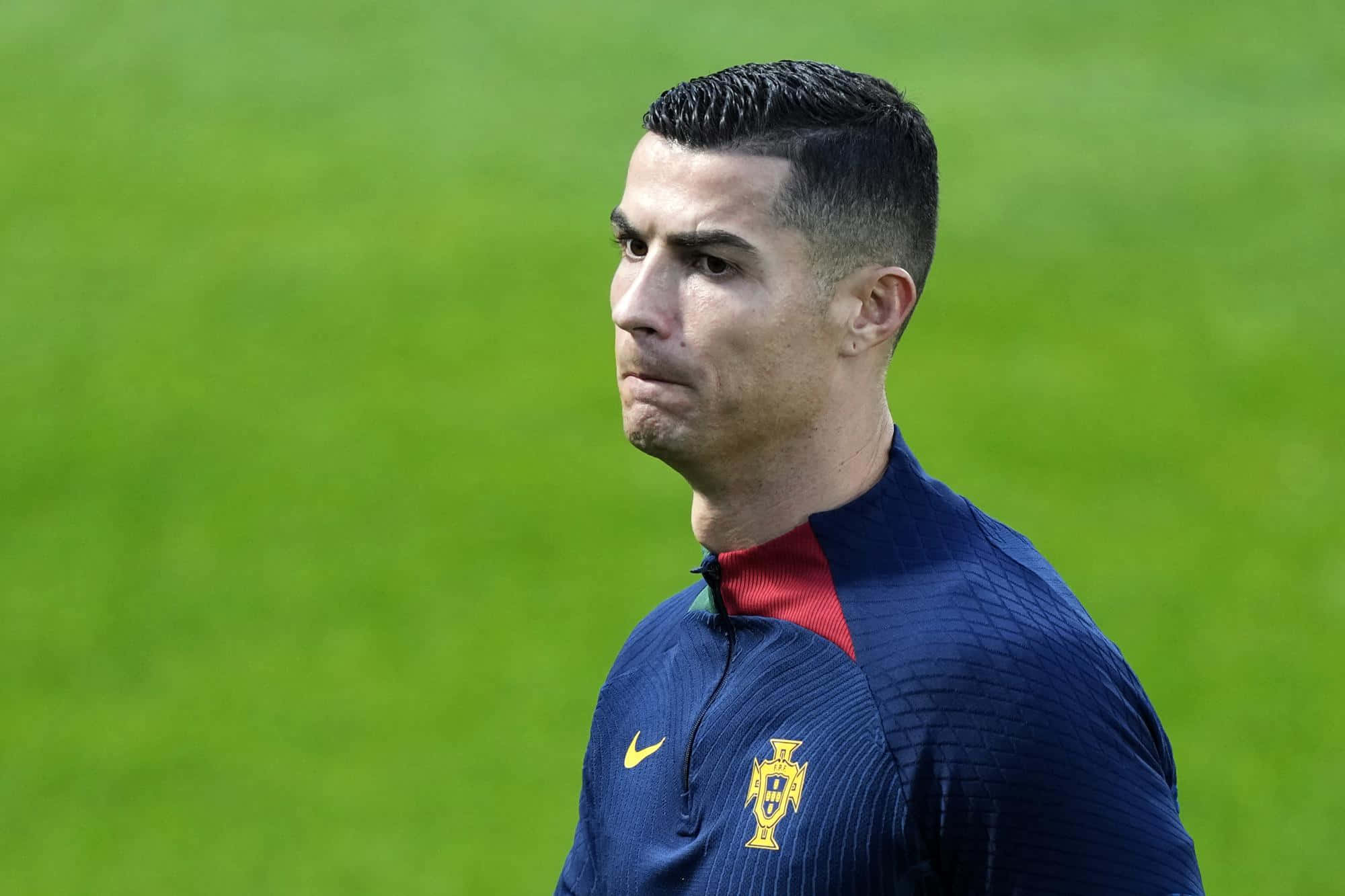 克里斯蒂亞諾·羅納度 桌布 壁紙 — Cristiano Ronaldo 身穿葡萄牙訓練球衣，在明亮的日光下專注地站在充滿活力的綠色足球場上。