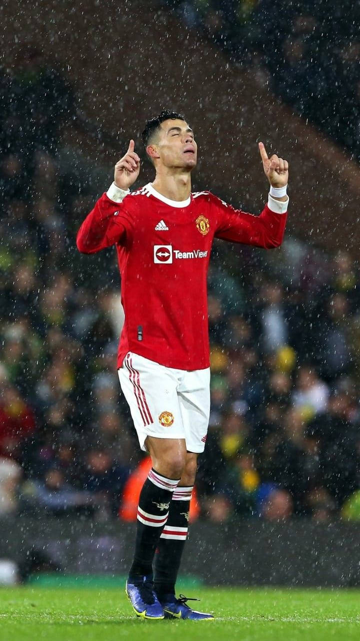 克里斯蒂亞諾·羅納度 桌布 壁紙 — Cristiano Ronaldo 在雨中穿著紅色曼聯球衣，在綠色球場上雙手指向天空慶祝。