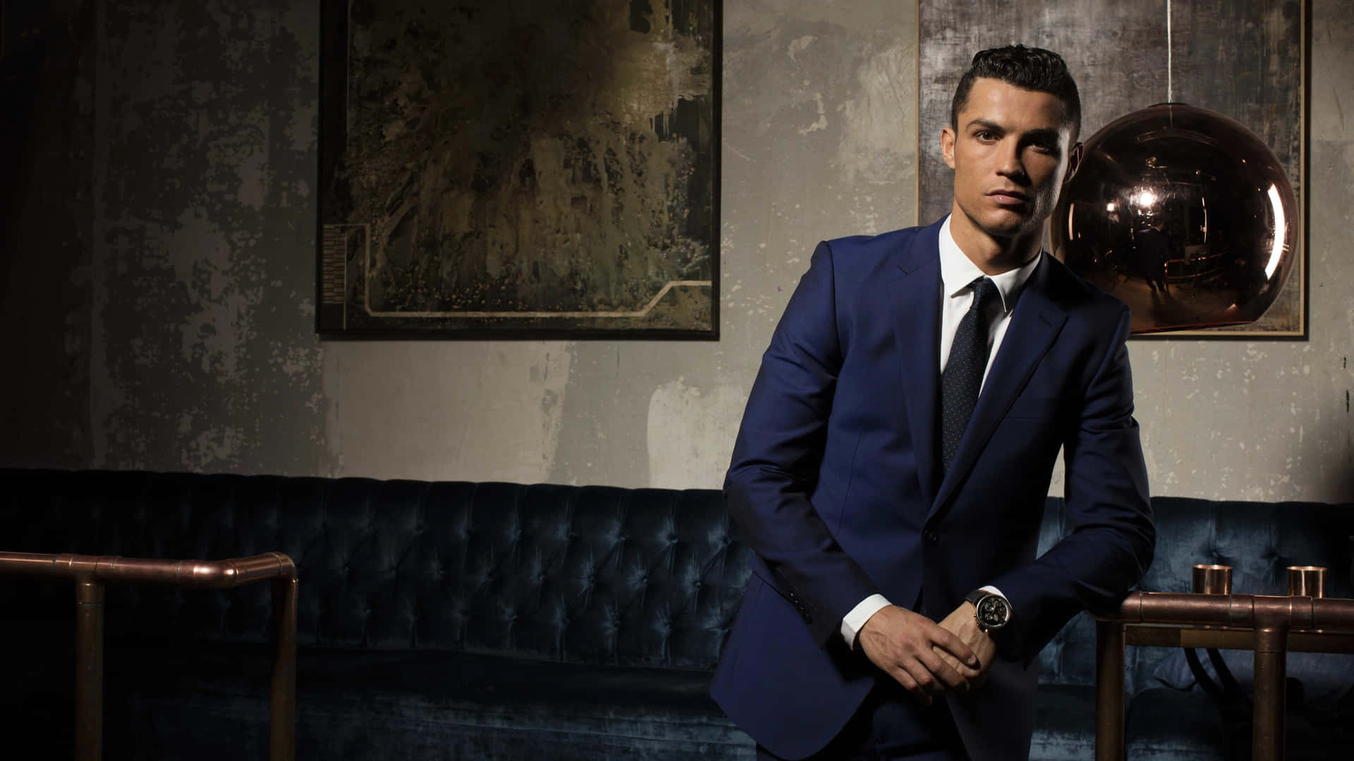  壁紙 — Cristiano Ronaldo 自信地穿著一件俐落的藍色西裝，背景是帶有復古藝術品和銅製地球儀的紋理牆壁。