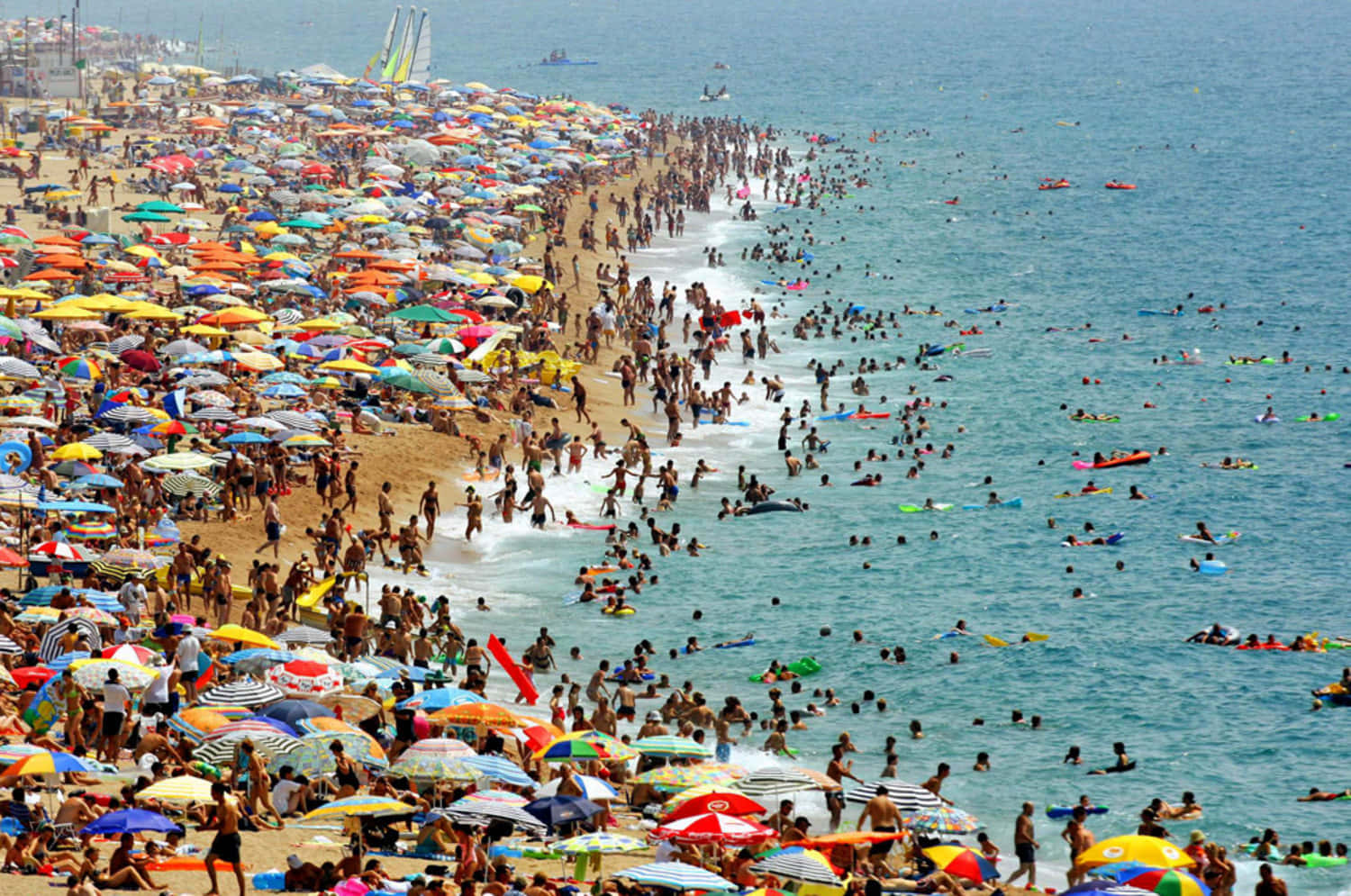 Mediterranean Beach 桌布 壁紙 — 一個擠滿色彩繽紛遮陽傘和享受碧綠海水的人們的海灘，在明亮的夏日陽光下。