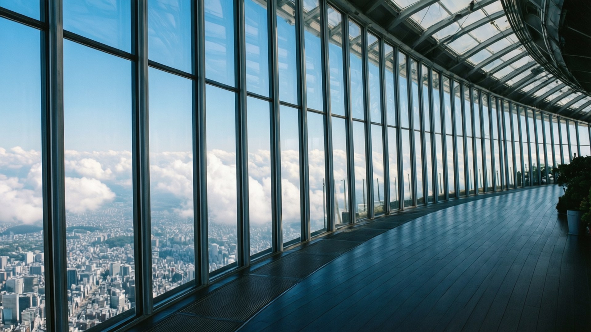Sky Garden Panorama 壁紙 — 一個彎曲的玻璃牆觀景台俯瞰著廣闊的城市景觀，坐落在蓬鬆的白雲之間，天空清澈湛藍。