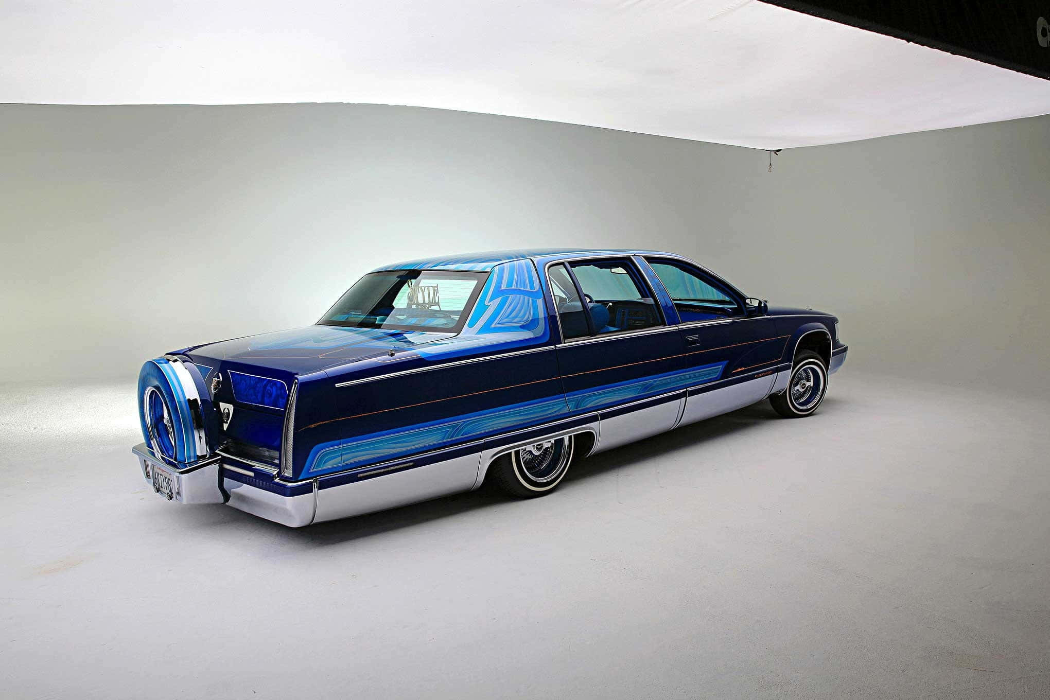 Cadillac Fleetwood 桌布 壁紙 — 一輛訂製的藍色低底盤汽車，帶有鍍鉻裝飾和噴繪條紋，在明亮的攝影棚中拍攝。