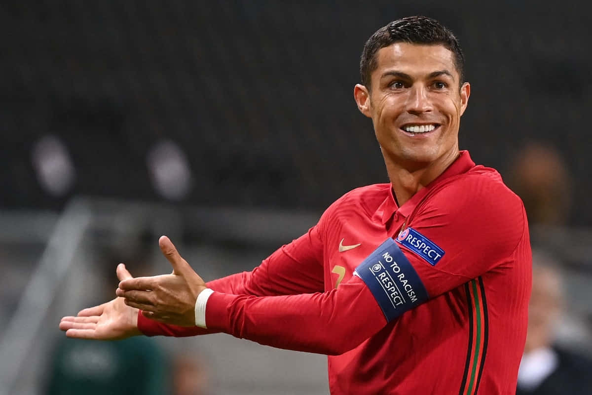 Ronaldo 桌布 壁紙 — C羅身穿紅色葡萄牙球衣，在球場上張開雙臂，露出溫暖的笑容。