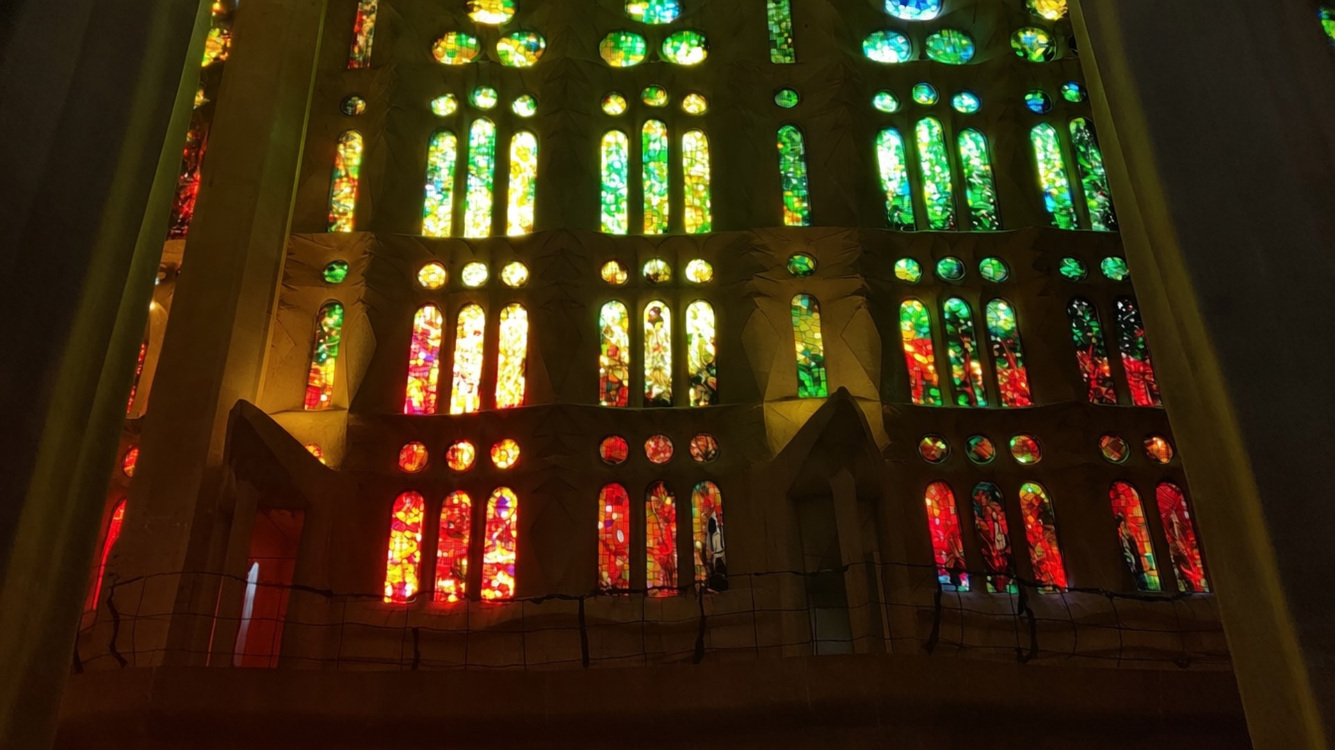 Sagrada Familia Light Show 壁紙 — 大教堂的彩色玻璃窗閃耀著鮮豔的紅、綠、黃色調，透過複雜的圖案投射出色彩繽紛的光線。