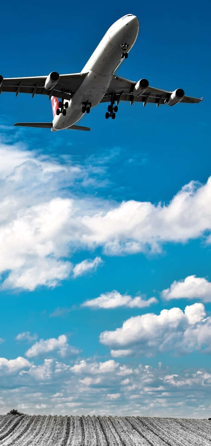  壁紙 — 一架大型客機放下起落架，在白雪覆蓋的田野上空，對著點綴著蓬鬆白雲的鮮豔藍天下降。