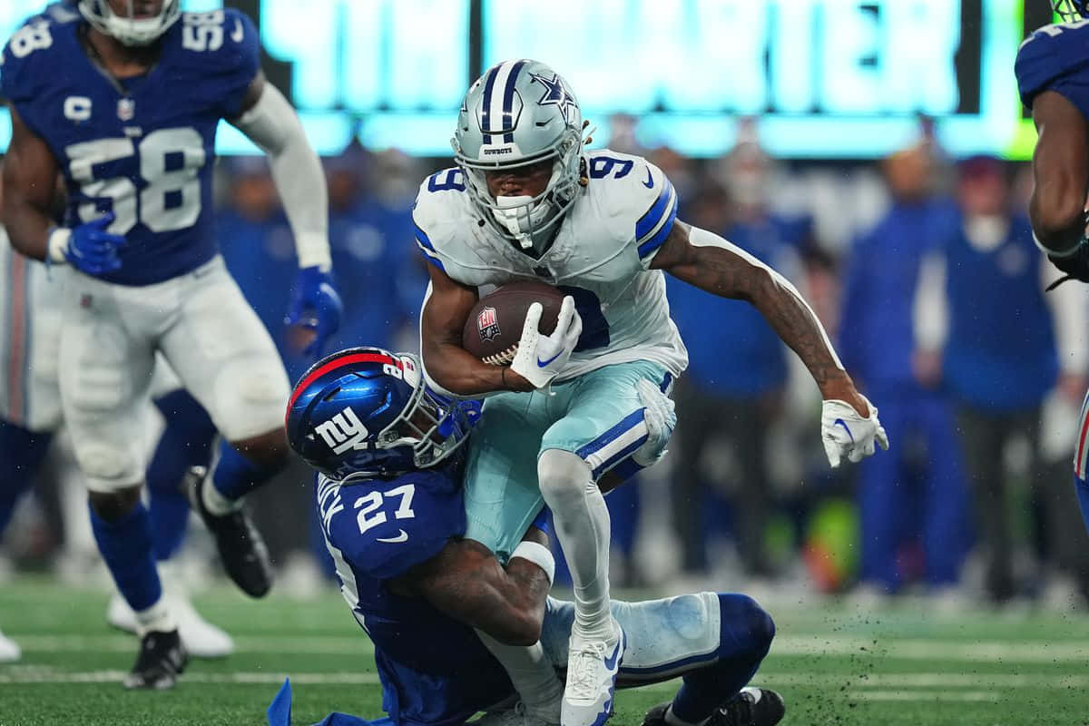  壁紙 — 達拉斯牛仔隊球員在一場高風險的NFL比賽中，緊抱橄欖球跳過一名飛身撲救的紐約巨人隊防守球員。